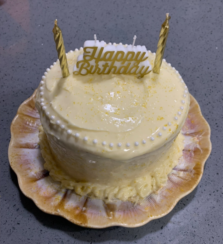 a white circular cake with pearls and a happy birthday candle