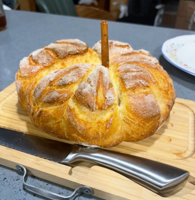 Bread in the shape of a pumpkin with a cinnamon stick acting as a stem